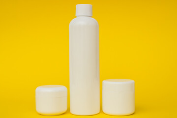white plastic cosmetic jars and cream on a yellow background