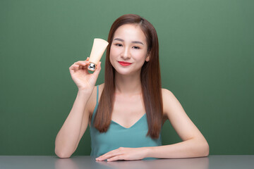 Attractive young Asian woman holding and showing cream tube product over green background.