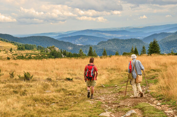 Naklejka premium Two friends hiking in a beautiful mountain environment. Older gentleman and younger friend talk peacefully in beautiful nature. A harmonious walk through the Romanian countryside in the evening.