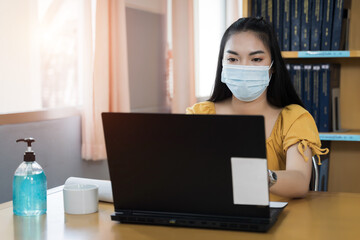 Fototapeta na wymiar A teenager student wears surgical mask and studies online via laptop during COVID-19 pandemic. University student girl watches online classes and writing a syllabus in notebook. Stock photo.