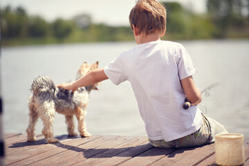 Boy sitting on a wood pier and enjoying with his dog and fishing.