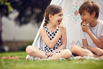 Summer time fun. Kids playing at backyard in teepee and eats cookies. © luckybusiness