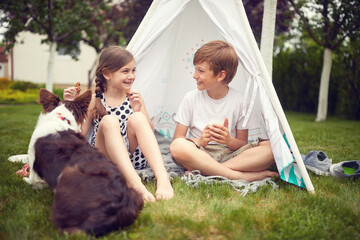  Children playing at backyard with dog in teepee and eats cookies.