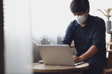 Coronavirus. Young asian man working from home wearing protective mask. Asia men in quarantine for coronavirus wearing protective mask. Working from home. Man using laptop for online working at home.