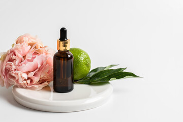 Glass brown bottle with serum and a pipette for skin care on a light background with peony flowers and lime. The concept of health and beauty. minimalism