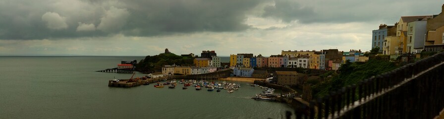 Panoramic view of Tenby, a coastal harbor town in southwest Wales. Image shows the harbor as well as the old town. The old town has traditional buildings with colorful facades.
