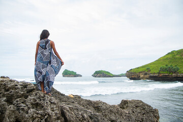 back view of woman wearing ethnic dress standing at the edge of the cliff at Kasap beach, Pacitan, East Java, Indonesia