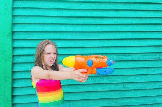 Girl with a water gun. Wooden background.