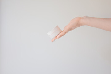 Round flacon for cream or lotion in female hand. Skincare and beauty concept. Mockup, copy space on a white background