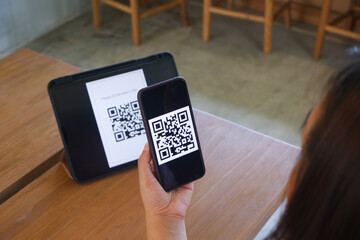 Women's hand uses a mobile phone application to scan QR codes in stores that accept digital...