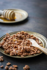 Knuspriges Granola mit Schololade und Honig auf einem goldenen Teller, rustikaler Hintergrund, Nahaufnahme, Frühstück