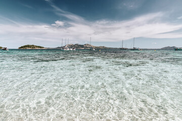 Fototapeta na wymiar Beautiful cristal clear water scene in Formentor beach Majorca, seascape with an island coast and sailboats on the horizon.