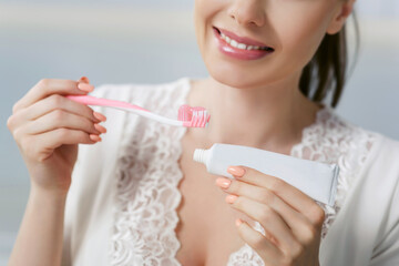 Young attractive woman squeezes toothpaste onto a brush. Morning oral hygiene at home. Girl in a...