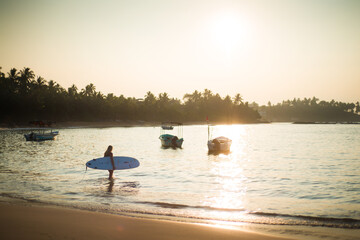 femme avec un surf au lever du soleil sur une plage du Sri Lanka