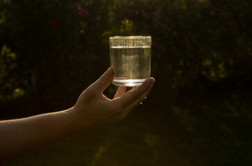 Sometimes a glass of water saves lives. A glass of water in the human hand in the sunset. Life...
