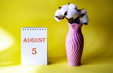 Calendar with text 5 august on yellow background and with a vase of flowers