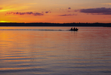 Fototapeta premium People vacationing in nature or fishermen go by boat on the lake during a beautiful sunset.