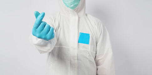 male standing in PPE suite and face mask doing mini heart hand sign on white background.