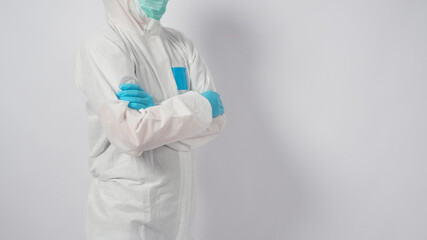 Male model is wearing PPE suite and face mask.He is standing and fold one's arms over the chest on white background.