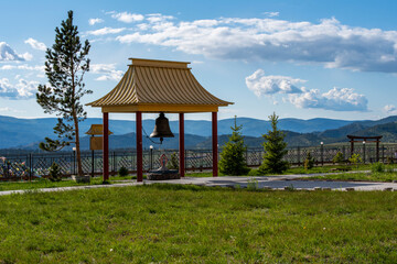 Fototapeta na wymiar pagoda with a bell in a Buddhist monastery on top of a mountain against a blue sky and green grass