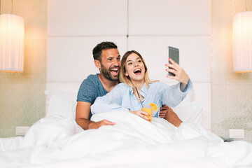 Young woman making selfie with her boyfriend on a bed in a hotel room
