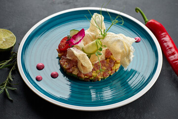 Salmon salad with avocado, on a blue striped plate, with lime,with chilli peppers, edible flowers, rosemary and chips