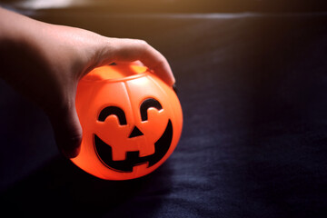 Scare hand holdung Halloween pumpkin head on black clothes in natural shadow and sunlight. Halloween holiday concept.