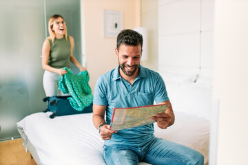 Happy couple packing suitcase and using map to search for travel trip
