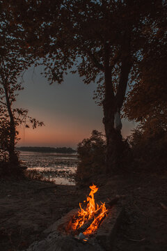 Bright orange glowing bonfire near a quiet river during evening sunset.