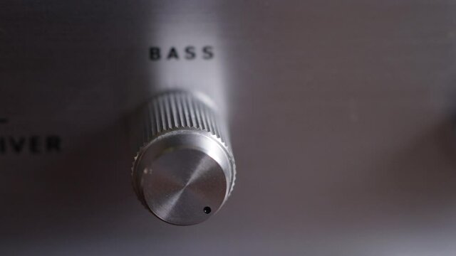Rack focus on a hand turning the bass knob on a vintage stereo all the way up