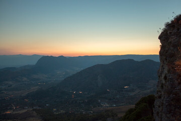 Panoramic aerial view of a italian valley from above, it is possible see trees and wood, with some road and mountain in background. Sunset moment