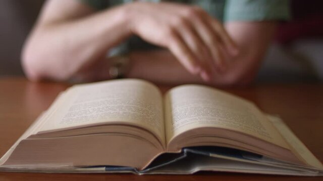 Close up of a person skimming the pages of a big book sitting at a desk