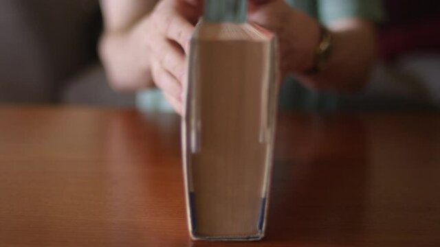 Close up on a book on a desk. A man out of focus closes it and leaves