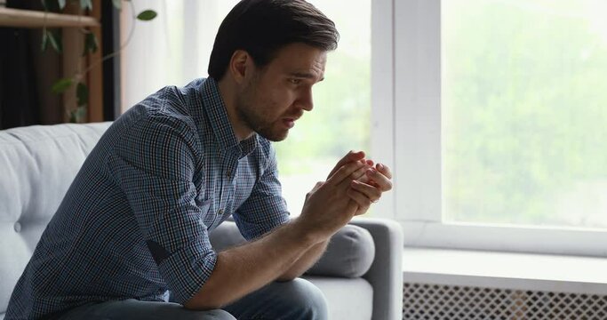 Disappointed young man sitting on couch thinking looking out the window feels moral badly after quarrel fight with wife, break up or divorce marriage split, unpleasant events in life suffering concept