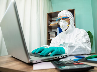 Disinfection man with special white suite working on laptop at office