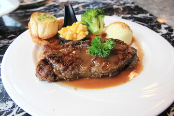 Pork steak with corn bread, broccoli and gravy in white disc on marble table.

