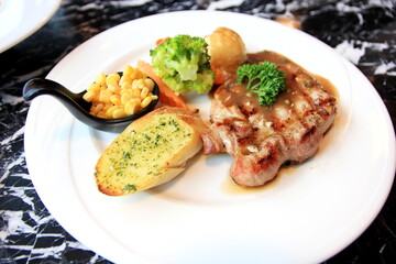 Pork steak with corn bread, broccoli and gravy in white disc on marble table.
