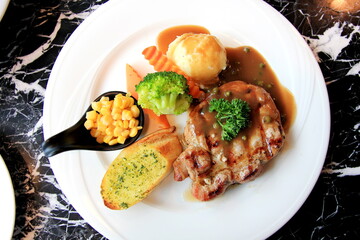 Pork steak with corn bread, broccoli and gravy in white disc on marble table.