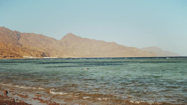 Man snorkeling in red sea, Beautiful landscape of blue sea and clear sky, waves crash against a stone coast and mountains on horizon Egypt, Dahab, full hd