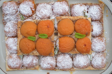 Ein Aprikosen-Blätterteig Kuchen auf eine Porzellan Platte. Ein Teil der Kuchen ist mit...