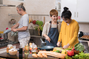 Happy Asian family of mother father and daughter cooking in kitchen making healthy food together feeling fun