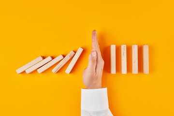 Hand of a businessman stopping domino effect on yellow background