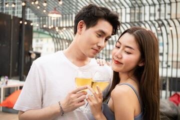 Lovely Asian young couple enjoy cheering white wine together in the valentines day party on roof top bar and restaurant at 5 stars hotel. Romantic Asia couple celebrating in valentines day together
