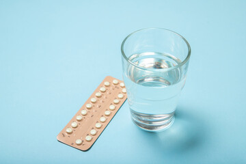 Female oral contraceptives and a glass of water on a blue background