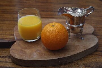 orange on a wooden board with orange juice and silver jug