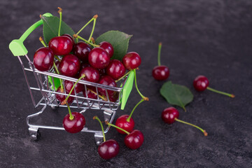 Small supermarket trolley with cherry on a black background.