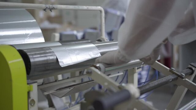 Factory worker taking finished product from machine. Unrecognizable Caucasian woman working on production line manufacturing aluminium foil rolls. Production, industry, business.