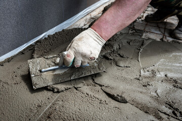 Construction worker troweling wet concrete on a top of concrete floor slab with steel wire mesh.