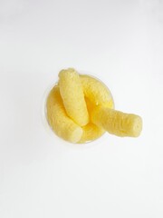 Yellow corn sticks in a transparent glass on a white background.
