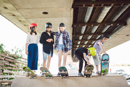 Group of friends children at skate ramp. Portrait of confident early teenage friends hanging out at outdoor city skate park. Little skateboarders posing with boards from above on ramp in skate park